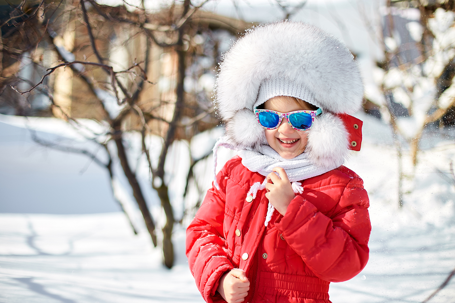 Happy laughing toddler girl wearing a red down jacket and white knitted hat and scarf