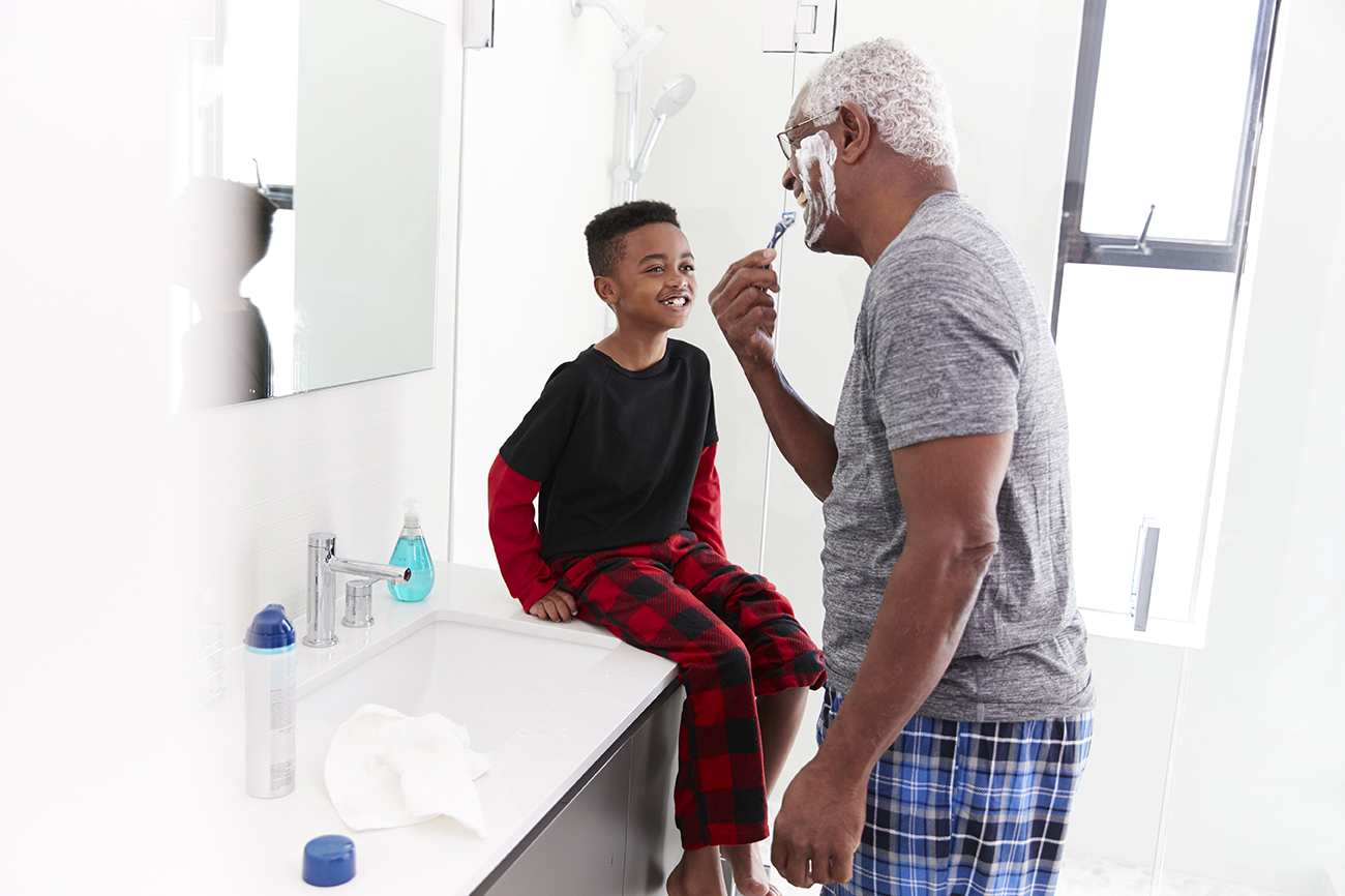 Man Pajamas In Bathroom Shaving Whilst Young man Watches